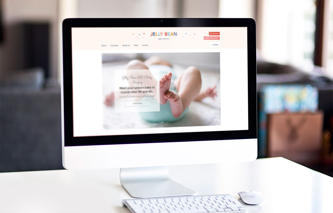 A computer monitor displays a website featuring a large photo of a baby’s feet and legs, with a form and text overlay on the image.
