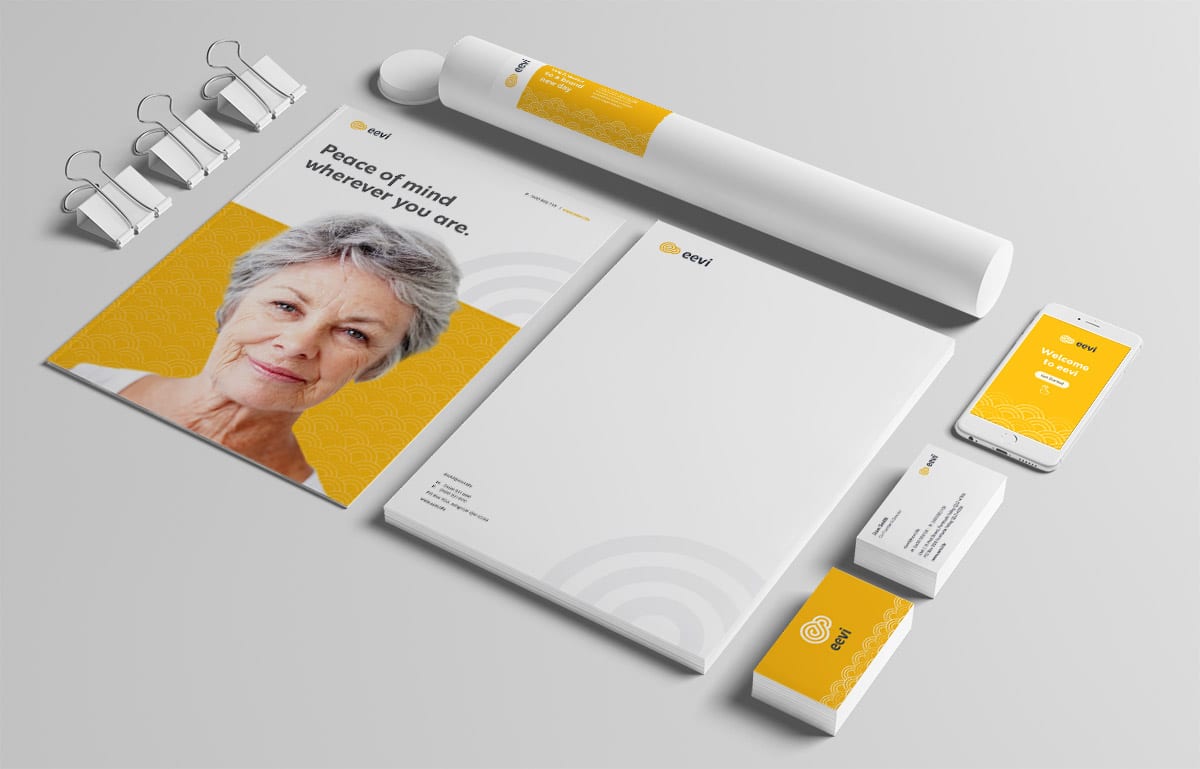 A stationery set with branded letterhead, business cards, brochure, document tube, phone, and binder clips, featuring a yellow and white colour scheme and an elderly woman on the brochure.